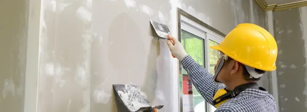 Worker applying joint compound to drywall near window